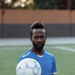 Portrait of a bearded African American man holding a soccer ball on an outdoor field.